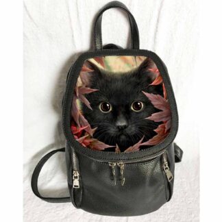 A cute black cat peers out through red and orange autumn leaves forming the front flap of this small backpack