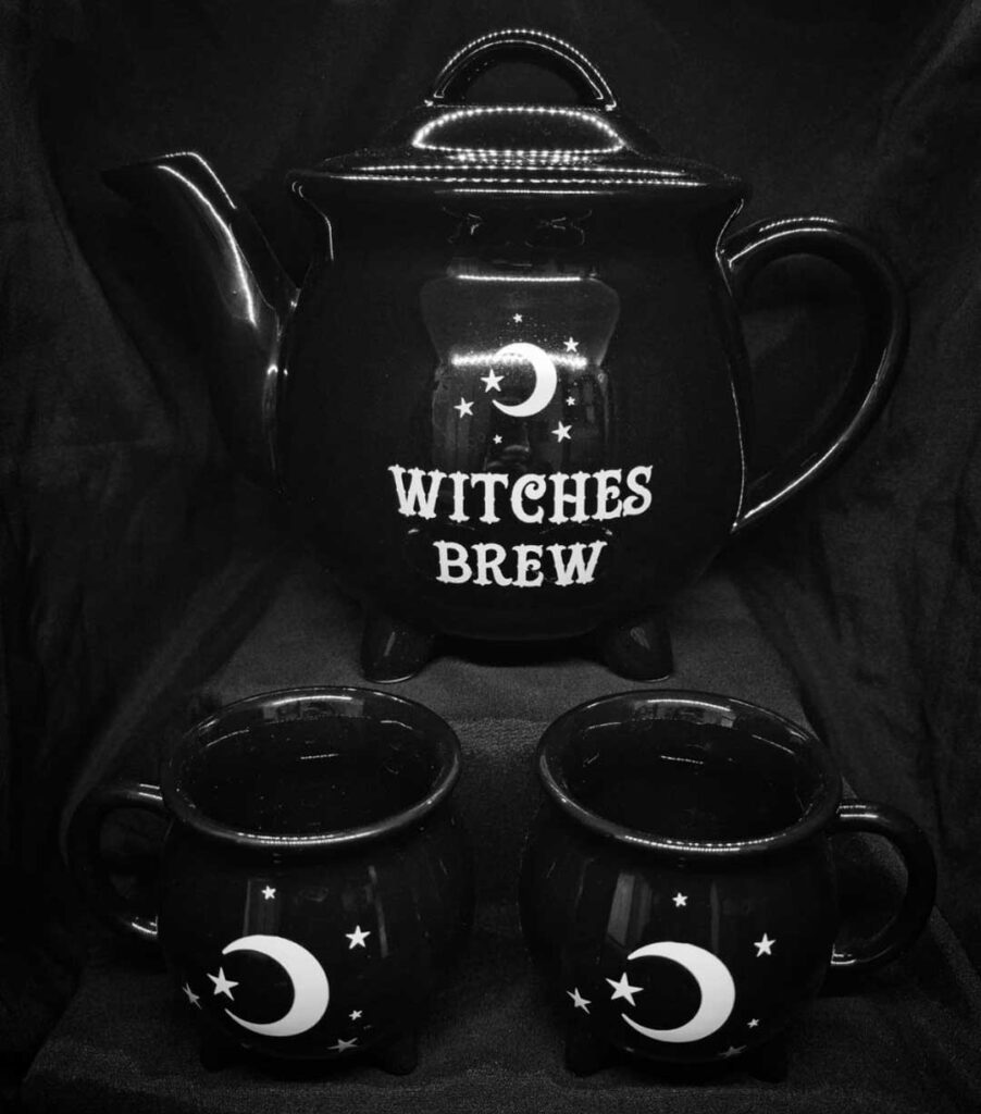 A black teapot with the words Witches Brew enscribed and two black mugs with moons printed on them