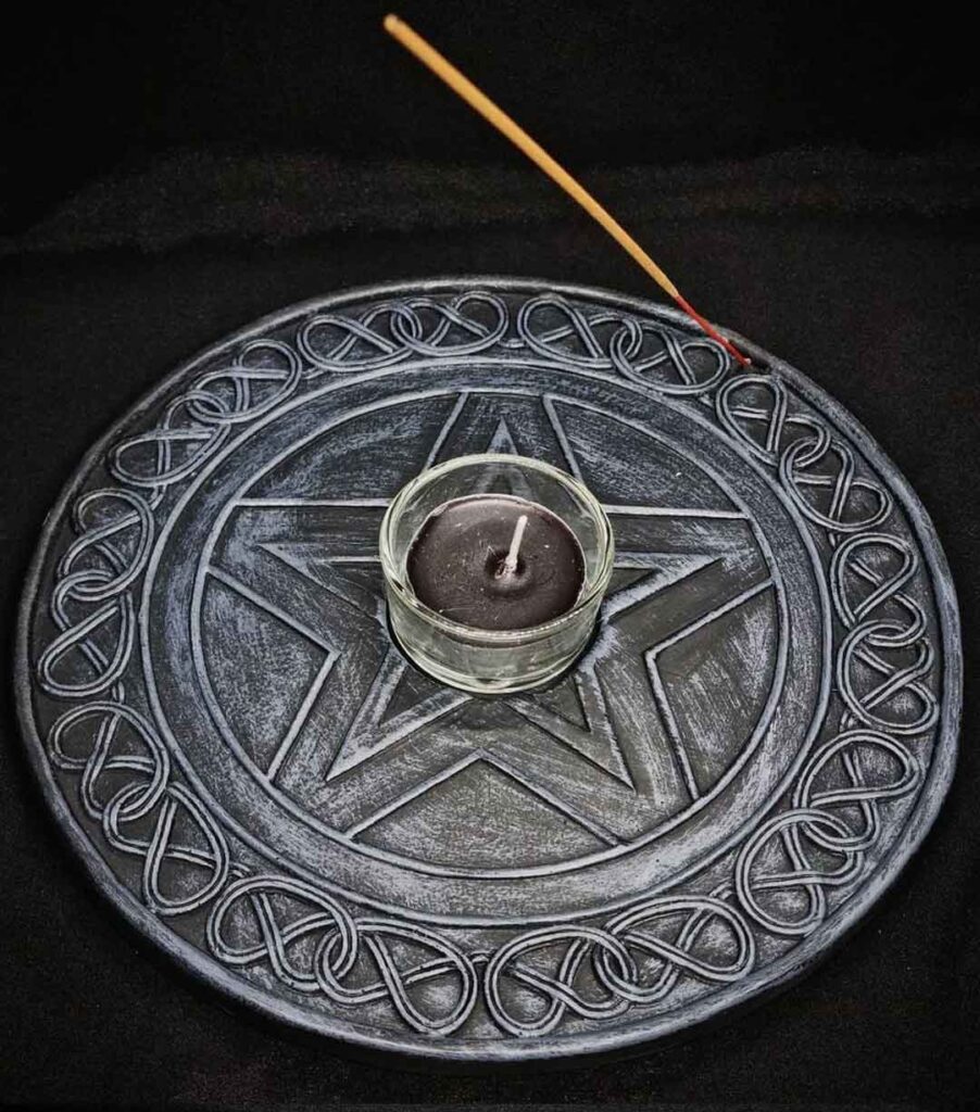 A grey tealight and incense holder enscribed with a pentagram and celtic patterns